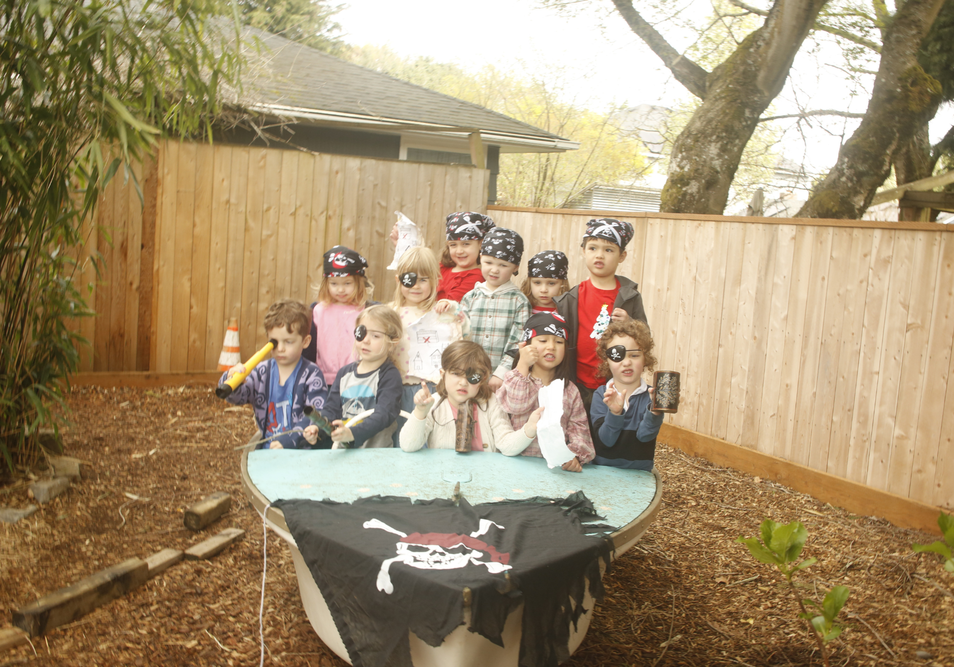 Group of children wearing pirate hats and eye patches gathered around an outdoor boat